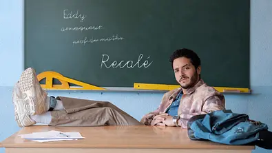 Der Lehrer Eddy aus der Netflix-Serie „Recalé“ sitzt an einem Schreibtisch. Hinter ihm an der Tafel steht der Name der Serie.  - Foto: Netflix