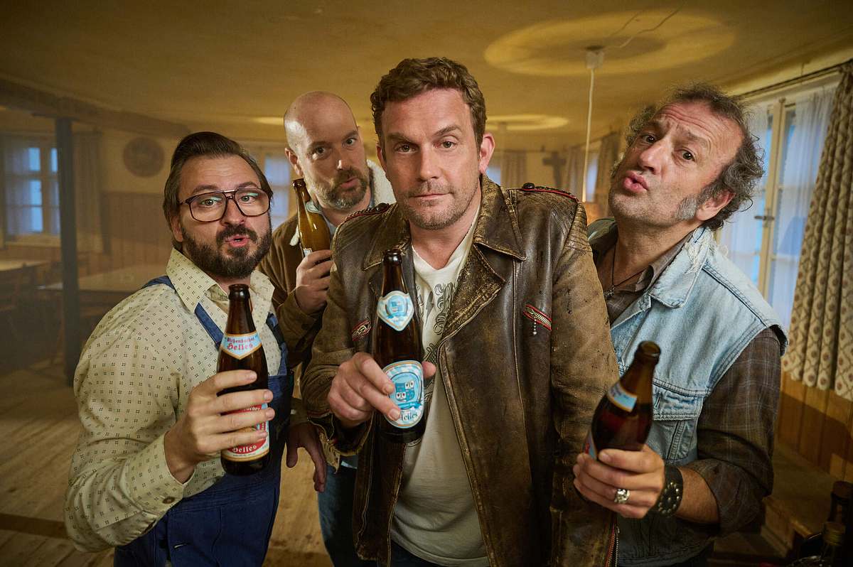 ARD-Krimi „Rehragout-Rendezvous“ Sebastian Bezzel und Kollegen in einer Szene aus „Rehragout-Rendezvous“, bayerische Krimi-Komödie mit Bier, Humor und skurrilen Charakteren.