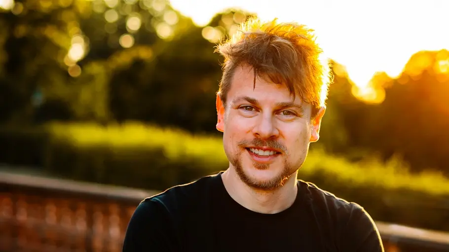 René steht vor einem Sonnenuntergang und lächelt