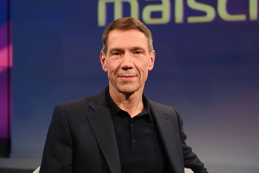 René Obermann Topmanager. René Obermann in dunklem Sakko und schwarzem Poloshirt sitzt vor einem blau-violetten Hintergrund mit angeschnittenem Schriftzug.