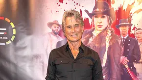 RIchard Norton im schwarzen Hemd steht vor einem Filmplakat mit einer Frau und mehreren Männern in Westernkleidung. - Foto: Imago/Future Image RIchard Norton im schwarzen Hemd steht vor einem Filmplakat mit einer Frau und mehreren Männern in Westernkleidung. - Foto: Imago/Future Image