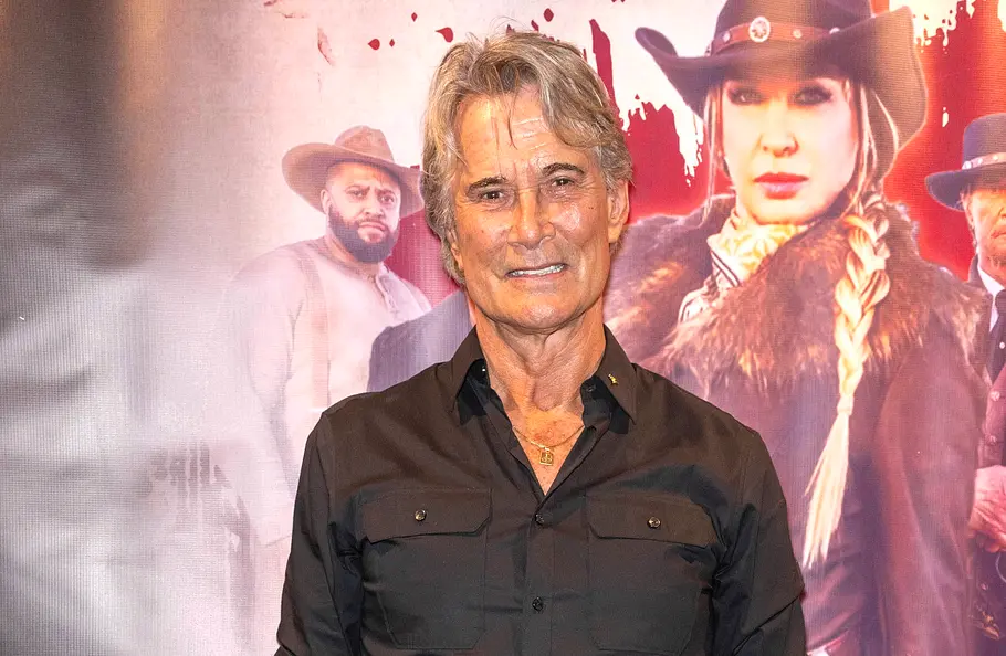Richard Norton Todesursache. RIchard Norton im schwarzen Hemd steht vor einem Filmplakat mit einer Frau und mehreren Männern in Westernkleidung.