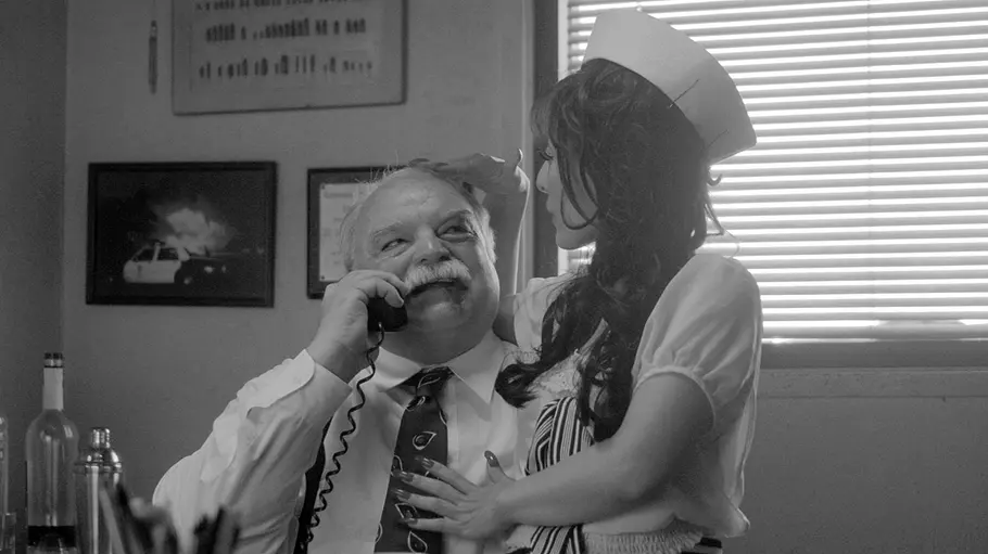 Richard Riehle ist tot Schwarz-Weiß-Bild: Schauspieler Richard Riehle hat in einer Szene des Films „Gone Doggy Gone“ eine Frau auf dem Schoß, während er telefoniert. Sie schauen sich an.