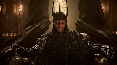 Sauron sitzt in dunkler Rüstung und mit einer hohen, spitzen Krone auf einem massiven Thron in einer dämmrigen Halle. - Foto: Prime Video Sauron sitzt in dunkler Rüstung und mit einer hohen, spitzen Krone auf einem massiven Thron in einer dämmrigen Halle. - Foto: Prime Video