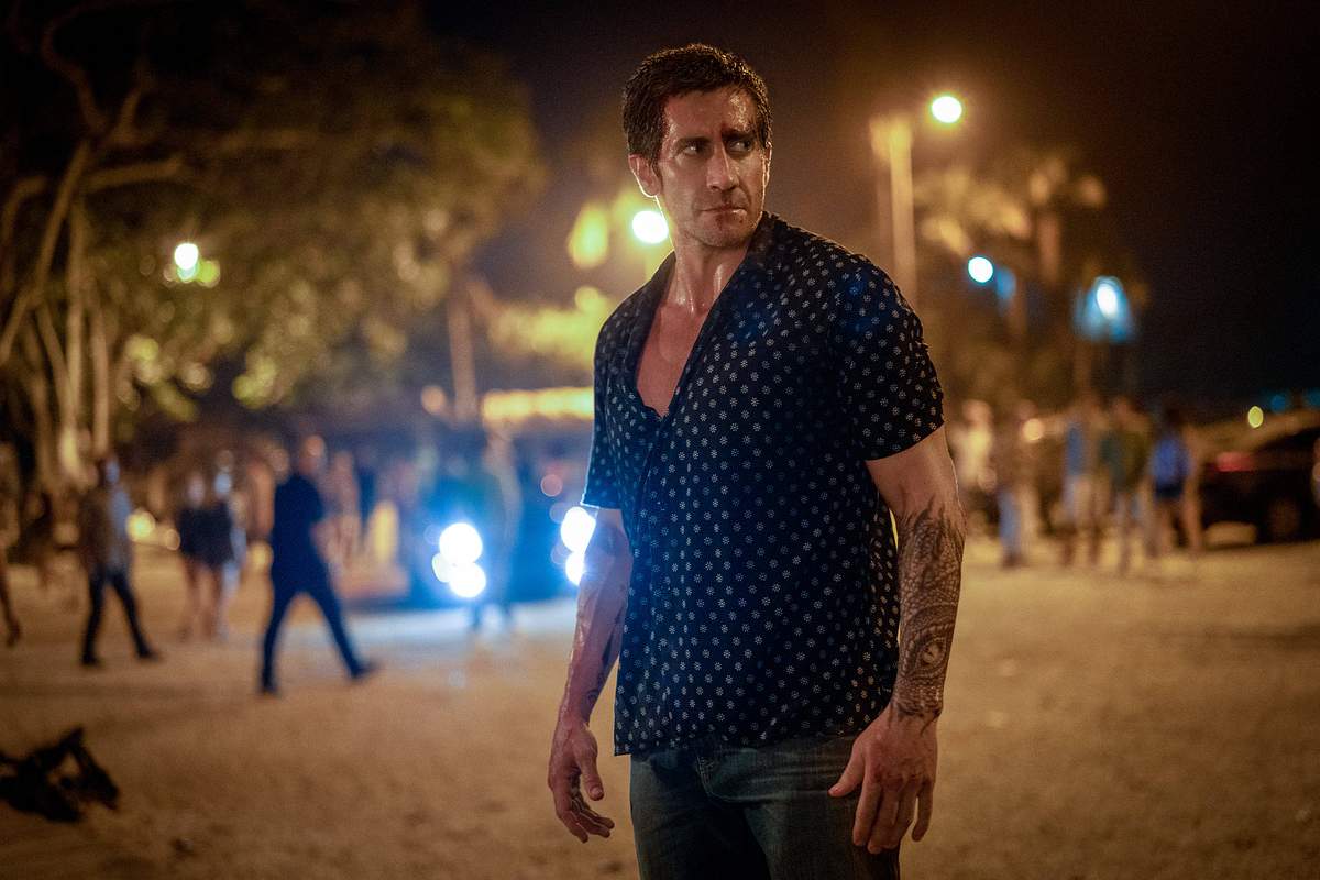 Jake Gyllenhaal steht auf einem Platz bei Nacht. Hinter ihm stehen mehrere Menschen. Er trägt ein dunkelblaues Hemd mit weißen Punkten.