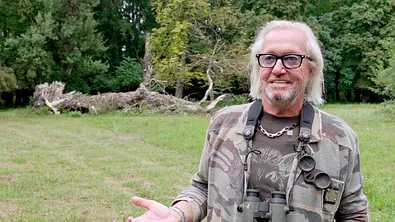 Robert Geiss aus „Die Geissens – Eine schrecklich glamouröse Familie“ steht mit Fernglas um den Hals auf einer Wiese und spricht in die Kamera. Im Hintergrund liegen ein umgestürzter Baum und dichter Wald. - Foto: RTLZWEI Robert Geiss aus „Die Geissens – Eine schrecklich glamouröse Familie“ steht mit Fernglas um den Hals auf einer Wiese und spricht in die Kamera. Im Hintergrund liegen ein umgestürzter Baum und dichter Wald. - Foto: RTLZWEI