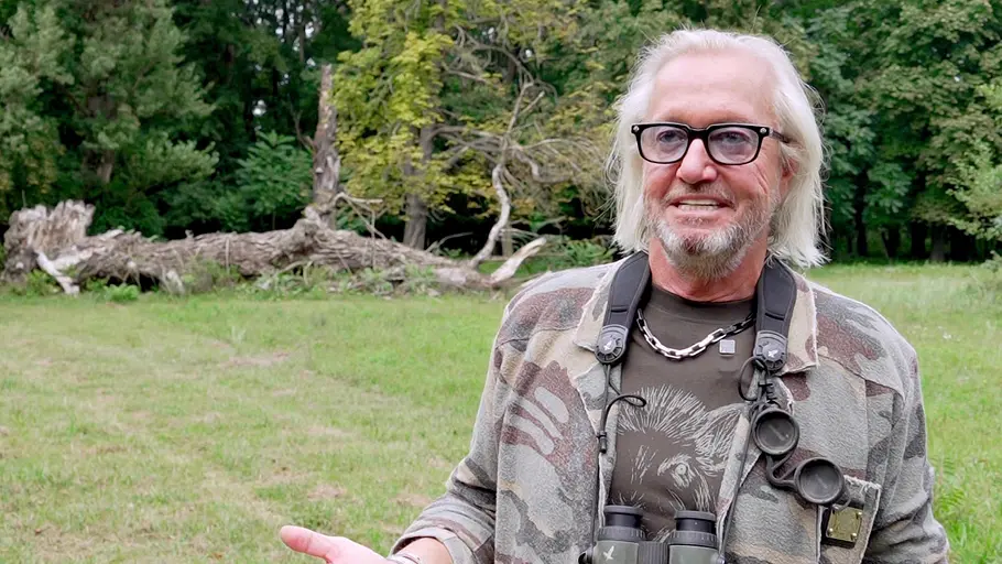Robert Geiss Robert Geiss aus „Die Geissens – Eine schrecklich glamouröse Familie“ steht mit Fernglas um den Hals auf einer Wiese und spricht in die Kamera. Im Hintergrund liegen ein umgestürzter Baum und dichter Wald.