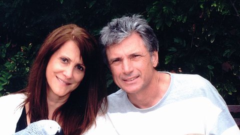 Robin Kaye und Thomas Deluca sitzen mit zwei Vögeln im Garten und lächeln in die Kamera. - Foto: Facebook//robin.kaye.10