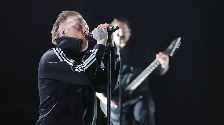 Sam Carter steht in einer schwarzen Adidasjacke vor dem Mikrofon und singt.