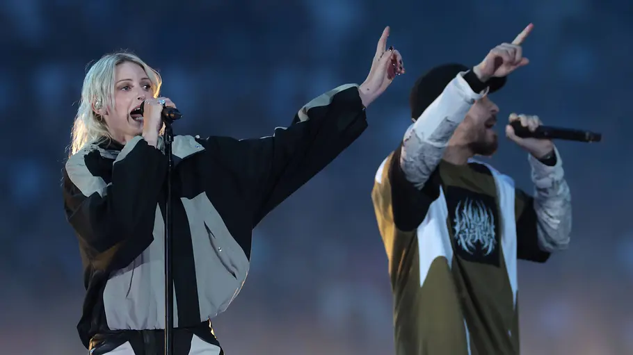 Emily Armstrong und Mike Shinoda auf der Bühne. Beide heben den Arm und haben ein Mikrofon in der anderen Hand.