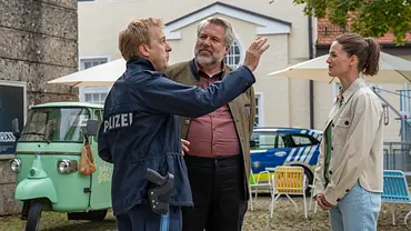  Polizeihauptmeister Mohr (Max Müller), Kommissar Stadler (Dieter Fischer) und Kommissarin Beck (Michaela Weingartner) stehen auf einem Platz beisammen. Im Hintergrund parkt ein dreirädriges mintfarbenes Fahrzeug, daneben stehen bunte Gartenstühle vor einem Polizeifahrzeug. Während Mohr mit dem rechten Arm gestikuliert, schauen ihm Stadler und Beck schmunzelnd zu. - Foto:  ZDF/Thomas Neumeier
