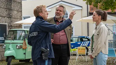 Polizeihauptmeister Mohr (Max Müller), Kommissar Stadler (Dieter Fischer) und Kommissarin Beck (Michaela Weingartner) stehen auf einem Platz beisammen. Im Hintergrund parkt ein dreirädriges mintfarbenes Fahrzeug, daneben stehen bunte Gartenstühle vor einem Polizeifahrzeug. Während Mohr mit dem rechten Arm gestikuliert, schauen ihm Stadler und Beck schmunzelnd zu. - Foto: ZDF/Thomas Neumeier Polizeihauptmeister Mohr (Max Müller), Kommissar Stadler (Dieter Fischer) und Kommissarin Beck (Michaela Weingartner) stehen auf einem Platz beisammen. Im Hintergrund parkt ein dreirädriges mintfarbenes Fahrzeug, daneben stehen bunte Gartenstühle vor einem Polizeifahrzeug. Während Mohr mit dem rechten Arm gestikuliert, schauen ihm Stadler und Beck schmunzelnd zu. - Foto: ZDF/Thomas Neumeier