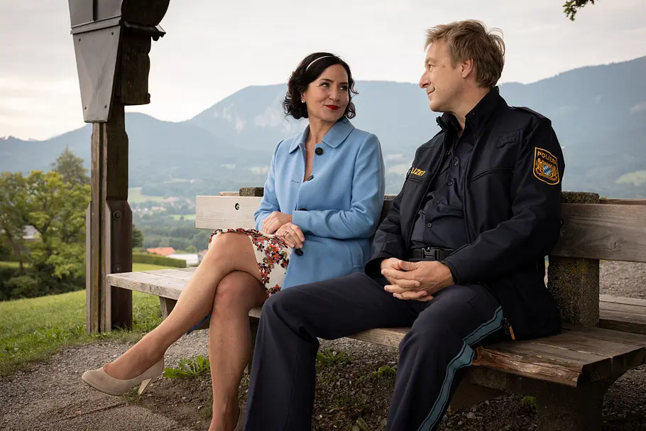 Miriam Stockl und Michael Mohr sitzen nebeneinander auf einer Holzbank und sehen sich lächelnd in die Augen.