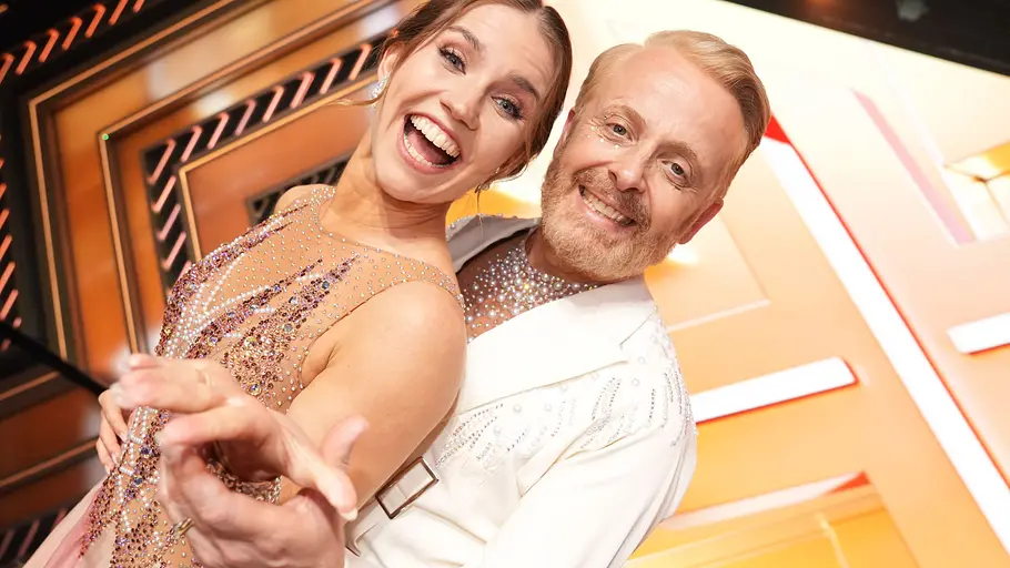 Ross Anthony und Mariia Maksina wollen sich nach vorne kämpfen. Ross Anthony und Mariia Maksina heben ihre Hand nach vorne und lachen.