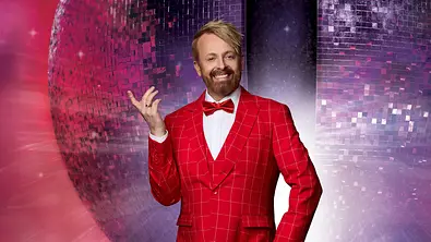 Ross Antony in einem auffälligen roten Anzug mit Fliege vor einer großen Discokugel, posierend im „Let’s Dance“-Look mit weißem Hemd und weißen Schuhen. - Foto: RTL / Jörn Strojny Ross Antony in einem auffälligen roten Anzug mit Fliege vor einer großen Discokugel, posierend im „Let’s Dance“-Look mit weißem Hemd und weißen Schuhen. - Foto: RTL / Jörn Strojny