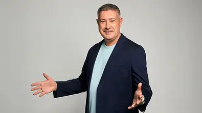Joachim Llambi in dunkelblauem Sakko und hellblauem T-Shirt steht mit ausgebreiteten Armen vor grauem Hintergrund. - Foto: RTL / Jörn Strojny