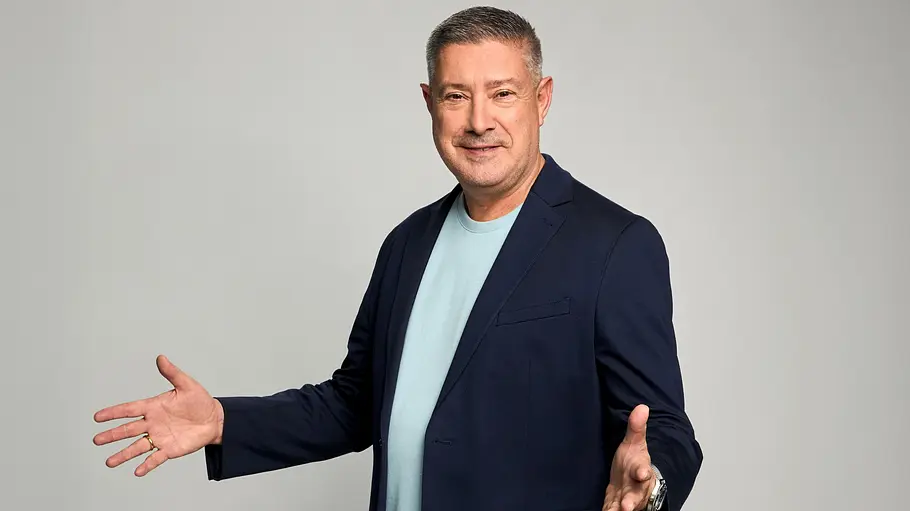 Joachim Llambi bekommt eine eigene RTL-Sendung. Joachim Llambi in dunkelblauem Sakko und hellblauem T-Shirt steht mit ausgebreiteten Armen vor grauem Hintergrund.