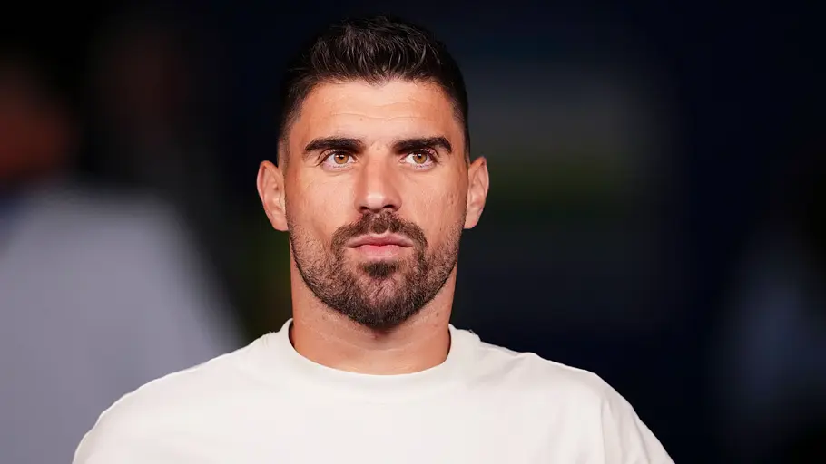 Fußballspieler der portugiesischen Nationalmannschaft in einem weißen Trainingsoberteil mit Verbandswappen blickt vor einem Länderspiel konzentriert nach vorne. Der Hintergrund ist dunkel und unscharf.