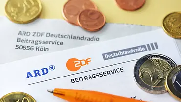 Euro-Münzen und ein orangefarbener Kugelschreiber liegen auf Unterlagen des Beitragsservice von ARD, ZDF und Deutschlandradio. - Foto: Imago/Christian Ohde Euro-Münzen und ein orangefarbener Kugelschreiber liegen auf Unterlagen des Beitragsservice von ARD, ZDF und Deutschlandradio. - Foto: Imago/Christian Ohde