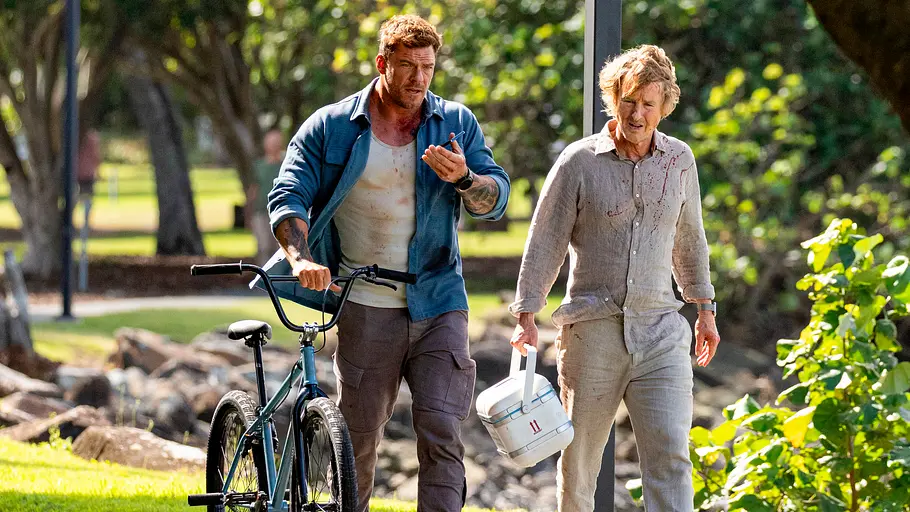 Hank und Ben gehen mit einem Fahrrad und einer Kühlbox durch einen Park.
