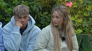 Ryan und Lina im Sommerhaus der Stars sitzen nebeneinander im Freien vor dichtem, grünem Buschwerk mit rosa Blüten.  - Foto: RTL