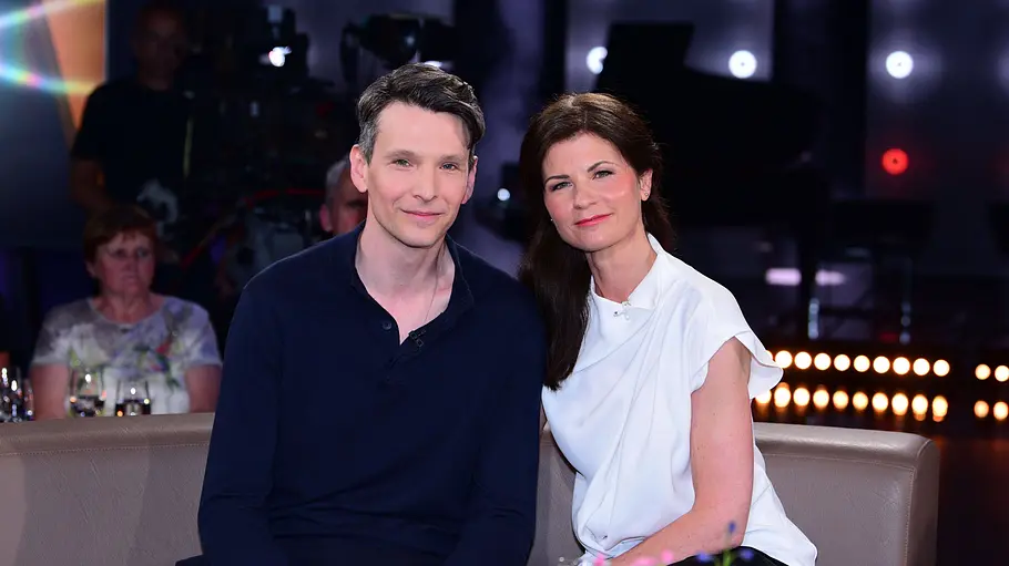 Sabin Tambrea, Schauspieler, und Alina Armonas-Tambrea, Musikerin Schauspieler Sabin Tambrea und Alina Armonas-Tambrea sitzen gemeinsam auf einem Sofa in einem TV-Studio und lächeln in die Kamera.