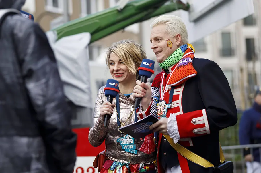 Sabine Heinrich und Guido Cantz beim Karneval. Sabine Heinrich und Guido Cantz stehen verkleidet für den WDR beim Rosenmontagszug in Köln vor der Kamera.