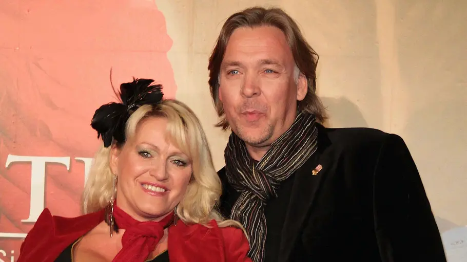 Sabrina Lange und Thomas Graf von Luxburg Sabrina Lange im roten Blazer und Thomas Graf von Luxburg im schwarzen Jackett mit karierter Hose posieren vor einem Plakat.