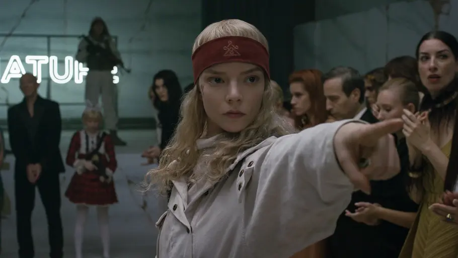 „Sacrifice“: Joan bringt die Charity-Gala unter ihre Kontrolle Anya Taylor-Joy trägt ein rotes Stirnband und eine helle Jacke. Sie zeigt mit ausgestrecktem Arm nach rechts; hinter ihr stehen Menschen.