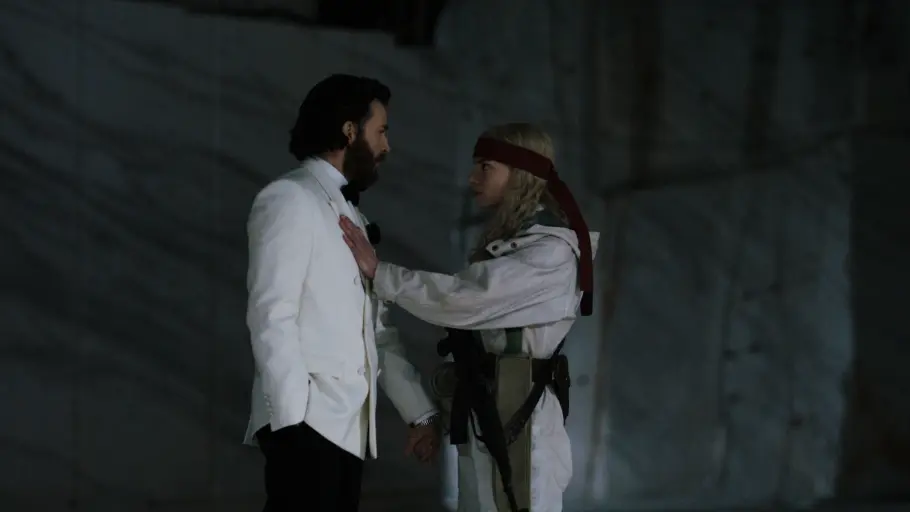 „Sacrifice“: Chris Evans gerät in Joans Gewalt Anya Taylor-Joy mit rotem Stirnband und Gewehr legt Chris Evans im weißen Jackett eine Hand auf die Brust.