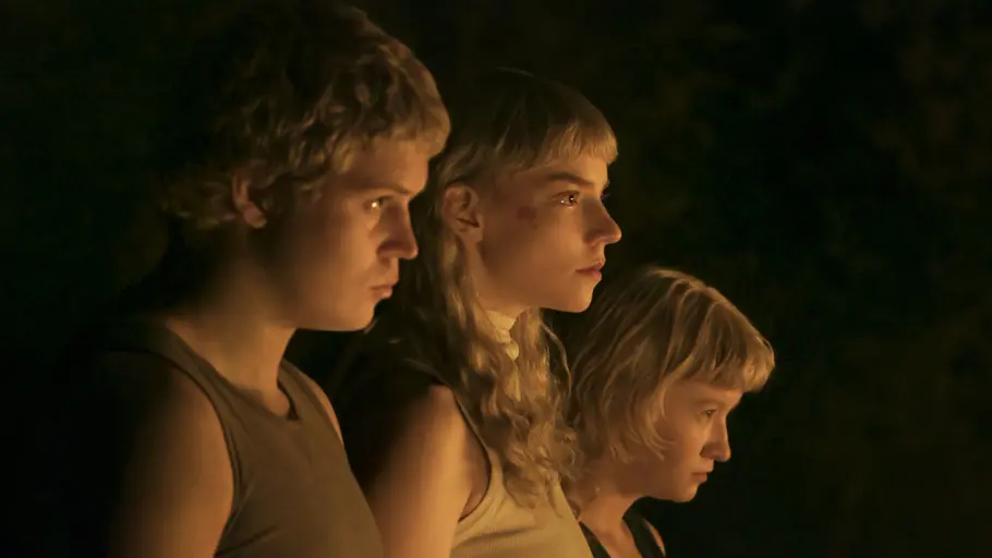 „Sacrifice“: Joan zieht mit ihren Geschwistern los Yung Lean, Anya Taylor-Joy und Jade Croot blicken im warmen Licht nach rechts. Der Hintergrund ist dunkel.