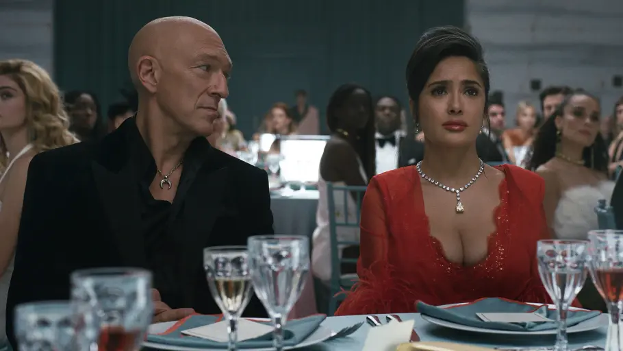 „Sacrifice“: Ben und Gloria Bracken laden zur Luxus-Gala Vincent Cassel im schwarzen Anzug und Salma Hayek im roten Kleid sitzen an einem gedeckten Tisch zwischen weiteren Gästen.