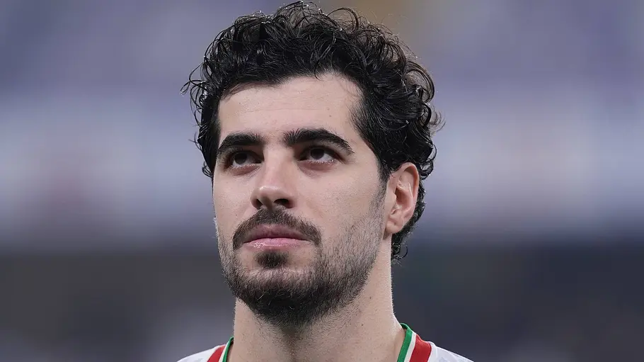 Iranischer Nationalspieler im weißen Trikot mit der Rückennummer 6 während der Nationalhymne vor einem Länderspiel. Er blickt konzentriert nach oben, der Hintergrund des Stadions ist unscharf.