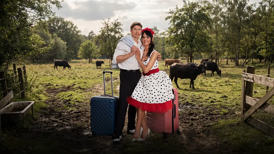 Sänger- und Künstlerpaar Giovanni Weisheit und Vanessa Neigert mit Koffern vor einer Kuhweide.