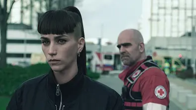 Julia schaut angespannt nach vorne, ein glatzköpfiger Mann hinter ihr schaut grimmig - Foto: JAIME OLMEDO / NETFLIX