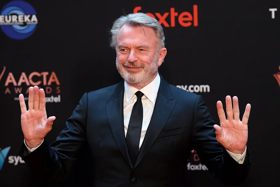 Sam Neill. Sam Neill mit erhobenen Händen.