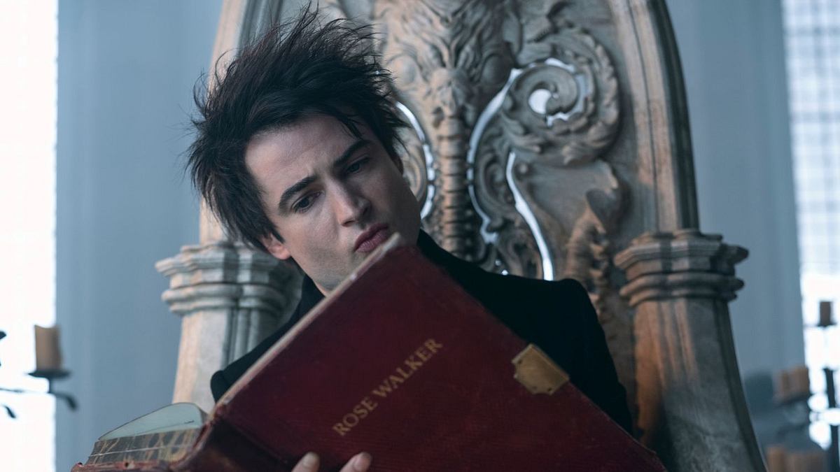 „Sandman“ auf Netflix endet früher als erhofft. Dream aus der Netflix-Serie „Sandman“ sitzt auf seinem Thron und ließt in einem roten, gebundenen Buch. Auf dem Cover steht „Rose Walker“.