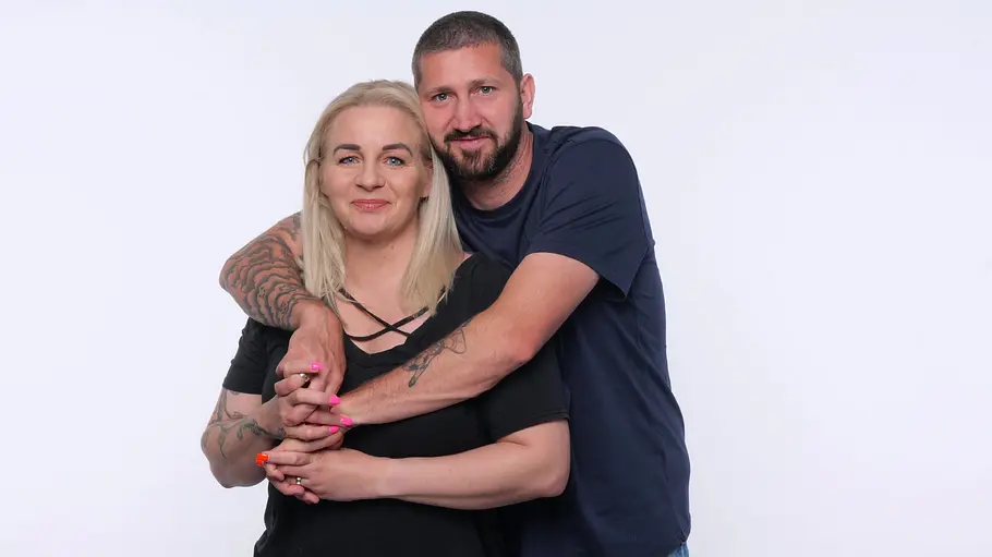 Sascha und Ivonne Mölders Sascha Mölders legt die Arme um Ivonne Mölders. Beide tragen dunkle Oberteile und Jeans und stehen vor hellem Hintergrund.
