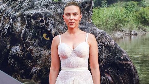 Scarlett Johansson steht in einem weißen Kleid vor einem „Jurassic World: Die Wiedergeburt“-Plakat und lächelt verschmitzt - Foto:  IMAGO / ABACAPRESS