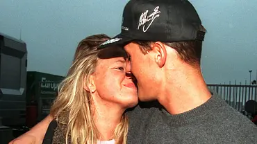 Michael Schumacher mit schwarzer Kappe küsst seine Ehefrau Corinna. Sie hält ein Buch mit einem Rennwagen auf dem Umschlag. - Foto: picture-alliance / dpa