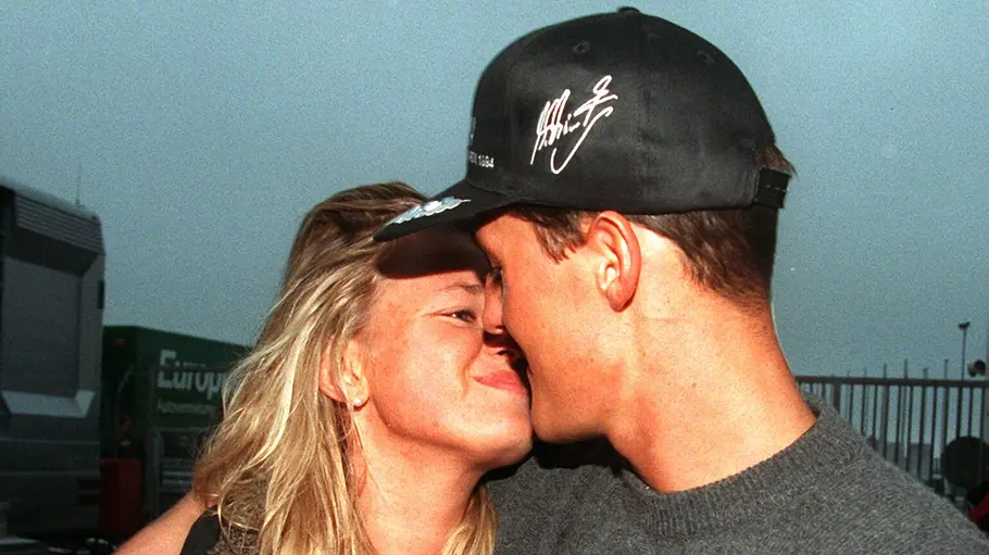 „Schumacher ’94“ zeigt Corinna und Michael knapp ein Jahr vor ihrer Hochzeit. Michael Schumacher mit schwarzer Kappe küsst seine Ehefrau Corinna. Sie hält ein Buch mit einem Rennwagen auf dem Umschlag.
