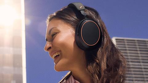 EIne Frau im Sonnenschein trägt lachend die Sennheiser Momentum 4 Wireless in der Special Edition. - Foto: © 2025 Sennheiser electronic SE & Co. KG