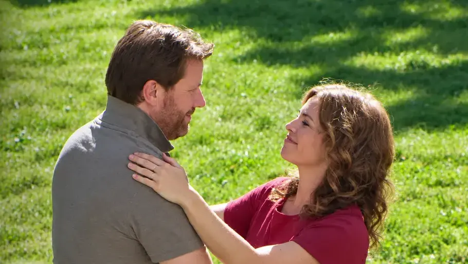 DIE LANDARZTPRAXIS-Vorschau FOLGE 87 Dienstag 27. Oktober Ella und Hanno halten einander auf einer Wiese im Arm. Links stehen das Logo „Die Landarztpraxis – Team Sonnenhof“ und ein Pfeil.