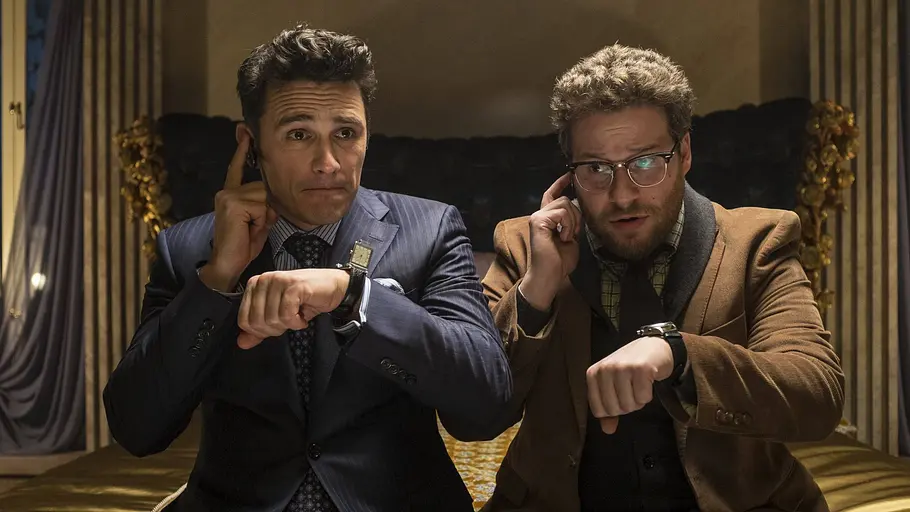 The Interview James Franco und Seth Rogen sitzen in Anzügen auf einem Bett, telefonieren und schauen auf ihre Armbanduhren.