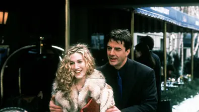 Sarah Jessica Parker (l.) und Chris Noth stehen vor verschiedenen Markisen. Parker trägt einen Pelzmantel.  - Foto: IMAGO / Capital Pictures