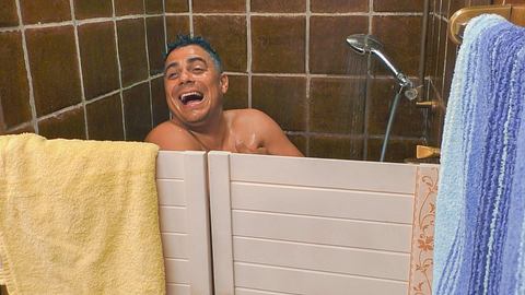 Silva Gonzalez in der Dusche beim Sommerhaus der Stars. Er steht hinter einer Holztür und lacht - Foto: RTL