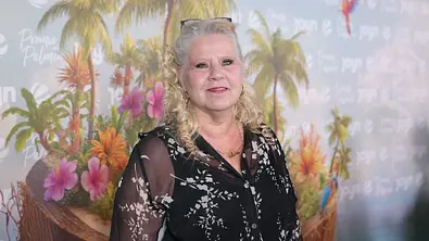 Silvia Wollny steht vor eine Fotowand der Sendung „Promis unter Palmen“.  - Foto: IMAGO / BOBO