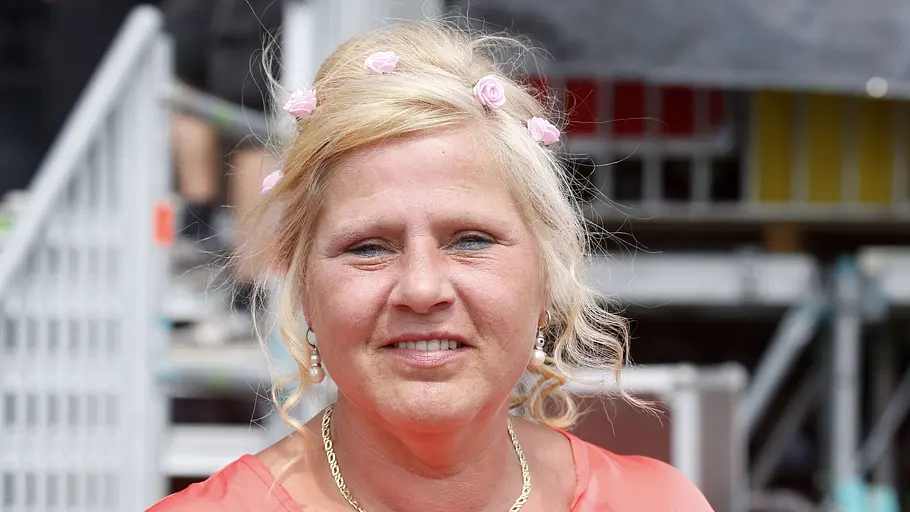 Silvia Wollny lächelt in die Kamera. Sie trägt einen Blumenkranz in den Haaren, eine goldene Kette und eine lachsfarbene Bluse.