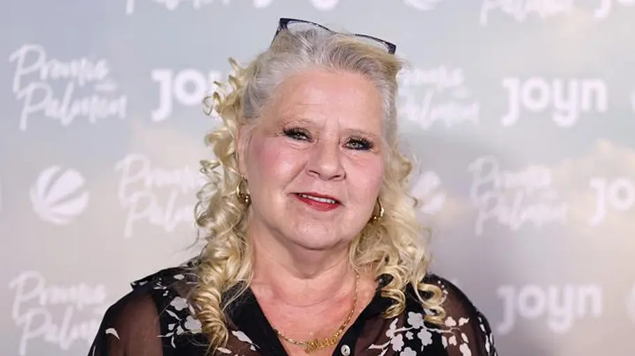 Silvia Wollny steht für „Promis unter Palmen“ vor einer Fotowand.