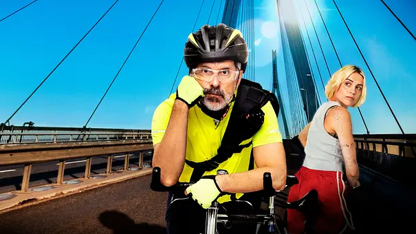 Bert (Christoph Maria Herbst) lehnt in neongelber Radkleidung auf einem Fahrrad. Les (Mala Emde) steht neben ihm auf einer Brücke. - Foto: © NDR/ARD/Westend61/Frizzi Kurkhaus Bert (Christoph Maria Herbst) lehnt in neongelber Radkleidung auf einem Fahrrad. Les (Mala Emde) steht neben ihm auf einer Brücke. - Foto: © NDR/ARD/Westend61/Frizzi Kurkhaus
